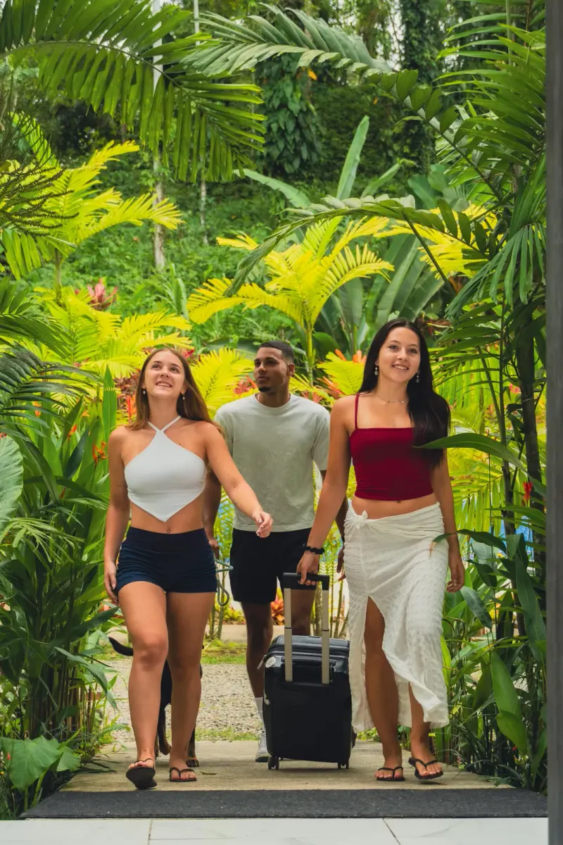 Three friends arriving with luggage through the garden