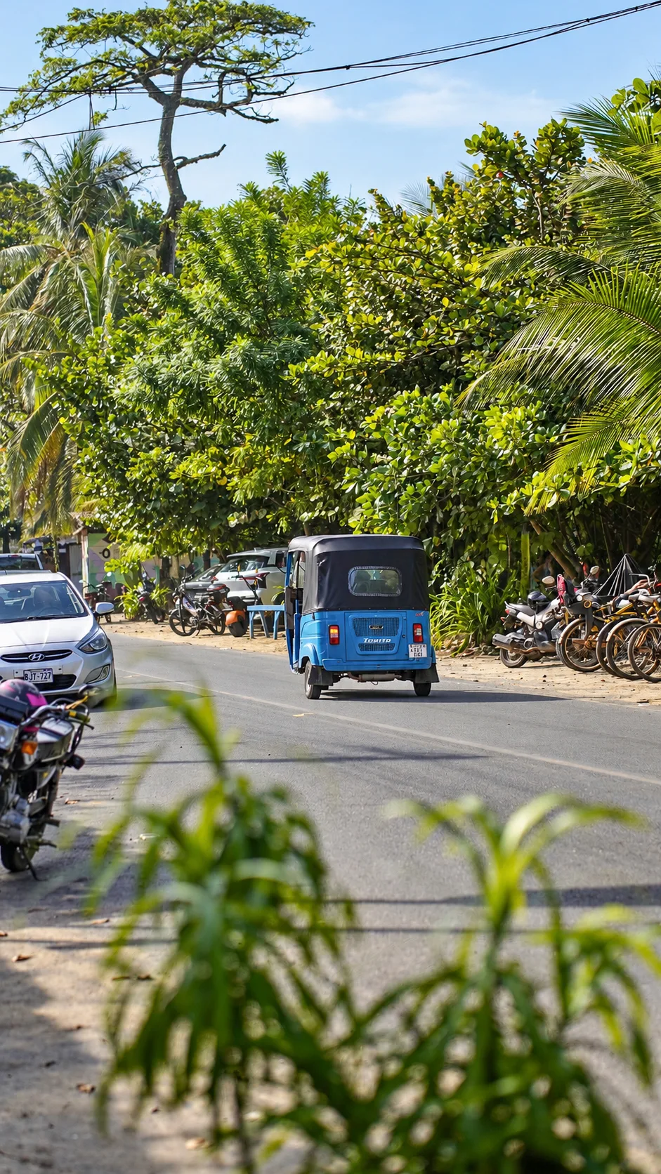 Blue tuk-tuk driving down the jungle-lined main road in Puerto Viejo, Costa Rica